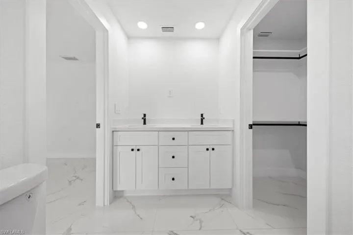 Bathroom with marble look tiles, a walk in closet, toilet, and recessed lighting