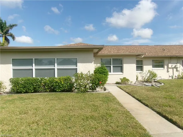 View of front of house with a shingled roof, a front yard, and stucco siding