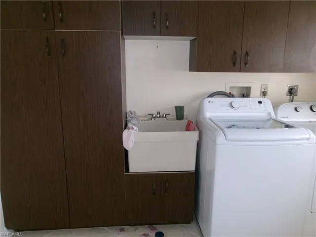 Laundry room featuring light tile patterned floors, separate washer and dryer, a sink, and cabinet space
