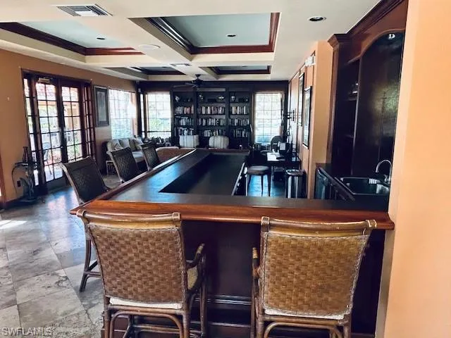 Bar area featuring dark countertops, french doors, coffered ceiling, ceiling fan, and crown molding