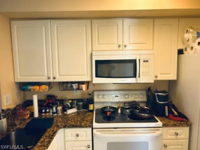 Kitchen with white appliances, white cabinets, and dark stone countertops