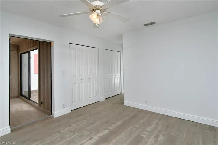 Master bedroom featuring two closets, ceiling fan, wood-style tile floors, textured ceiling and access to rear 4 season lanai