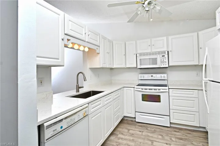 Kitchen with light wood-type tile flooring, white appliances, vaulted ceiling, sink and white cabinets