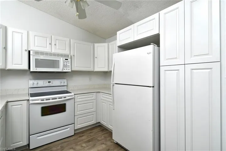 Kitchen with white appliances, tile / wood-style floors, white cabinetry, and lofted ceiling