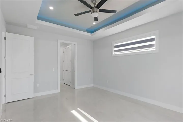 Spacious room featuring light-colored flooring, a tray ceiling with recessed lighting and a ceiling fan, and a window with blinds