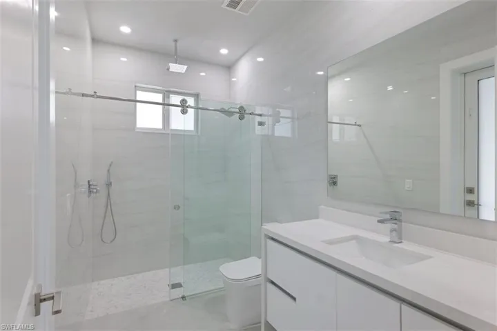 Bathroom featuring a modern vanity with an integrated sink, a large mirror, and a glass-enclosed shower with a rainfall shower head