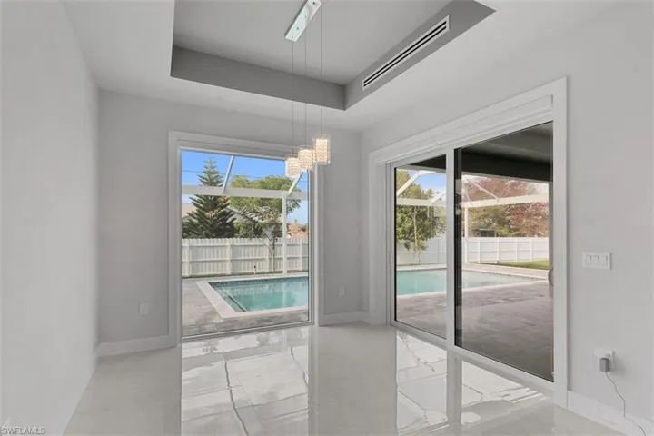 This bright room features glossy tile flooring, a modern chandelier, and a recessed ceiling detail
