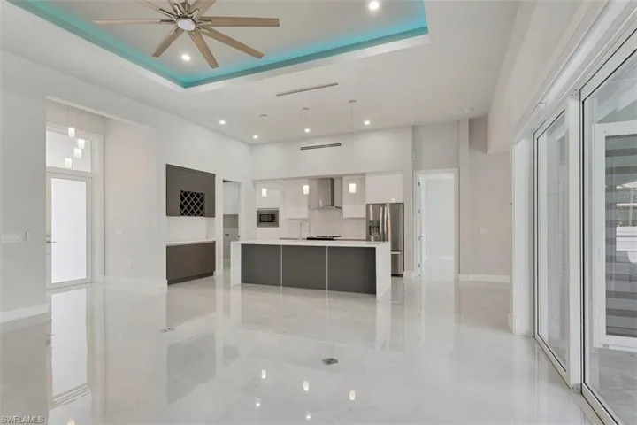 Open concept living area featuring polished light-colored flooring, a modern kitchen with a central island, and large sliding glass doors