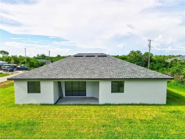 Back of house with stucco siding, a patio area, a yard, and a shingled roof