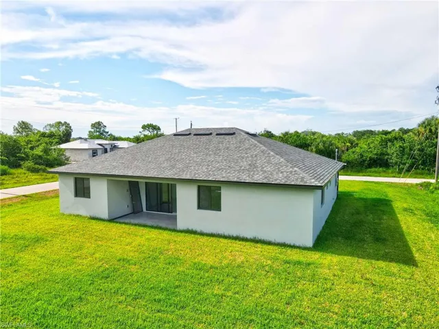 Rear view of house featuring a shingled roof, a yard, stucco siding, and a patio