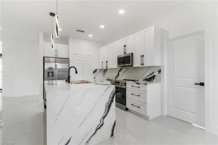 Kitchen with backsplash, light stone countertops, white cabinets, pendant lighting, and stainless steel appliances