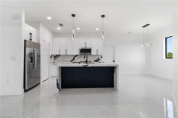 Kitchen with tasteful backsplash, decorative light fixtures, an island with sink, stainless steel appliances, and white cabinetry