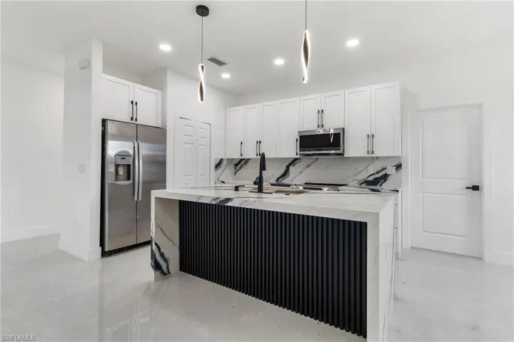 Kitchen featuring tasteful backsplash, appliances with stainless steel finishes, light stone countertops, white cabinetry, and hanging light fixtures
