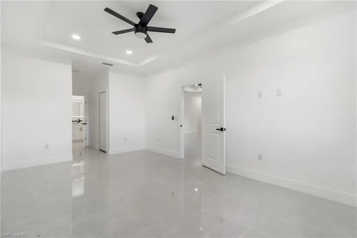 Unfurnished bedroom featuring a raised ceiling, recessed lighting, ceiling fan, and ensuite bath