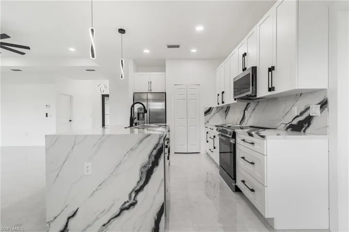 Kitchen with light stone counters, tasteful backsplash, white cabinetry, recessed lighting, and hanging light fixtures