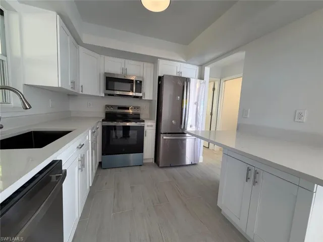 Kitchen with stainless steel appliances, white cabinets, light stone counters, and wood tiled floors