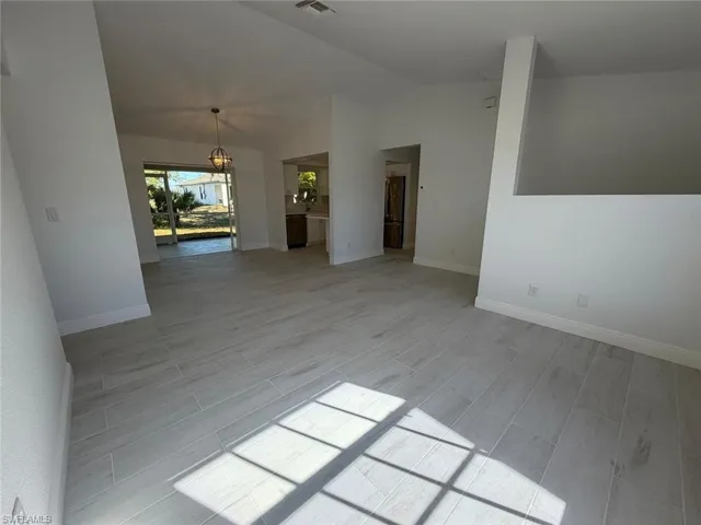 Empty room with lofted ceiling, wood tiled floors, and a chandelier