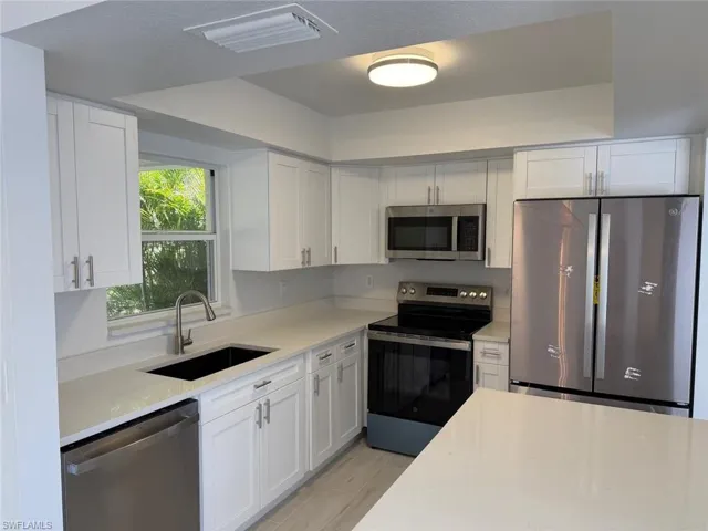 Kitchen featuring stainless steel appliances, white cabinetry, light stone countertops, and wood finish floors