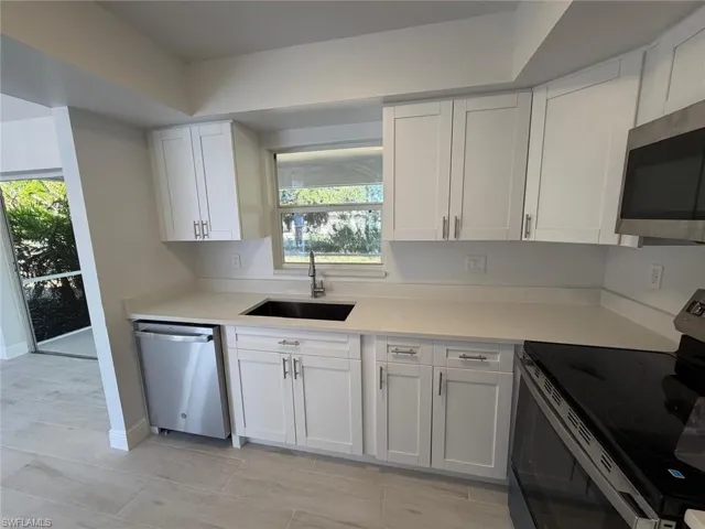 Kitchen featuring appliances with stainless steel finishes, white cabinets, light stone counters, and light tile patterned floors