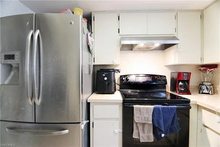 Kitchen with stainless steel fridge with ice dispenser, black / electric stove, under cabinet range hood, and light countertops