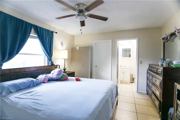 Bedroom with light tile patterned floors, ensuite bath, a textured ceiling, and a ceiling fan