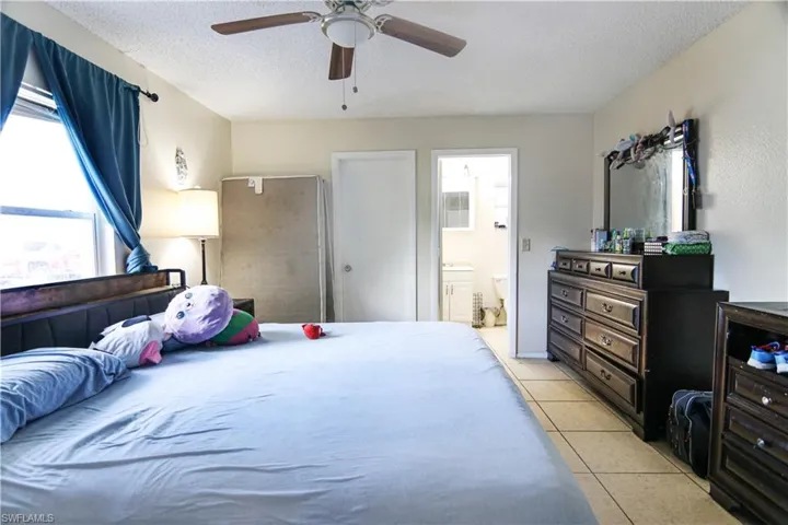 Bedroom featuring light tile patterned flooring, ensuite bathroom, a textured ceiling, and ceiling fan
