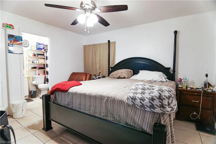 Bedroom featuring light tile patterned floors, ceiling fan, and ensuite bath