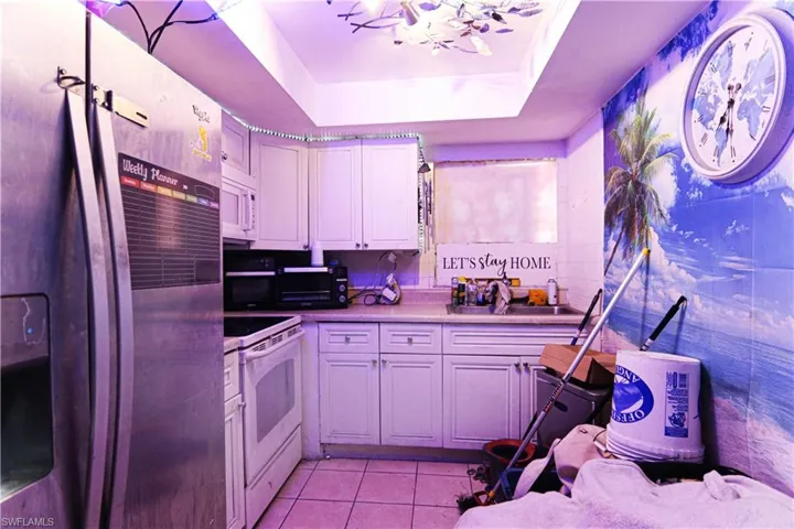 Kitchen with white appliances, light tile patterned flooring, a tray ceiling, and white cabinets