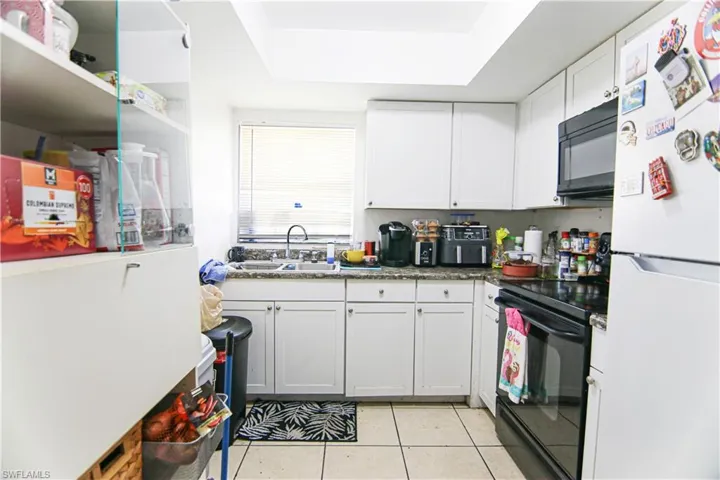Kitchen with black appliances, light tile patterned floors, white cabinetry, and a raised ceiling