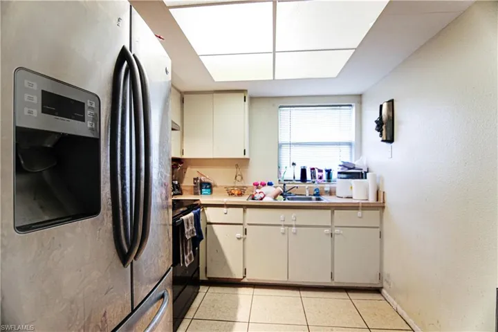 Kitchen with stainless steel fridge, black electric range, light countertops, light tile patterned flooring, and cream cabinets
