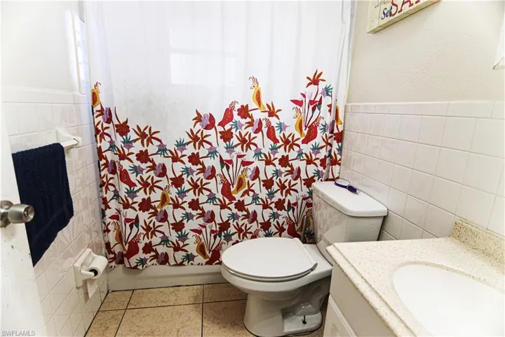 Bathroom with tile walls, vanity, curtained shower, a wainscoted wall, and tile patterned floors