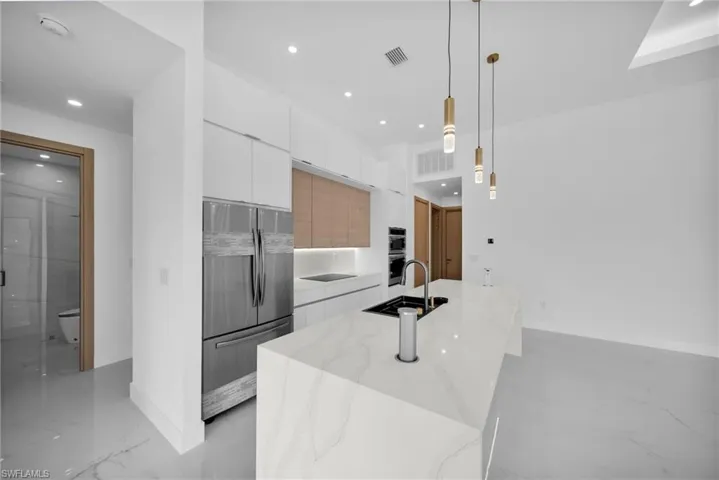 Kitchen featuring hanging light fixtures, white cabinets, an island with sink, sink, and appliances with stainless steel finishes