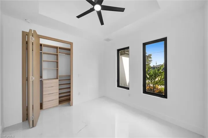 Unfurnished bedroom featuring tile patterned flooring, a tray ceiling, a closet, and ceiling fan