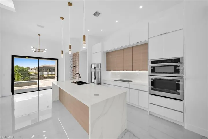 Kitchen with white cabinetry, stainless steel appliances, pendant lighting, a large island with sink, and sink
