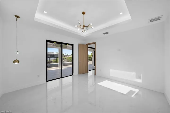 Tiled spare room with a raised ceiling and a notable chandelier