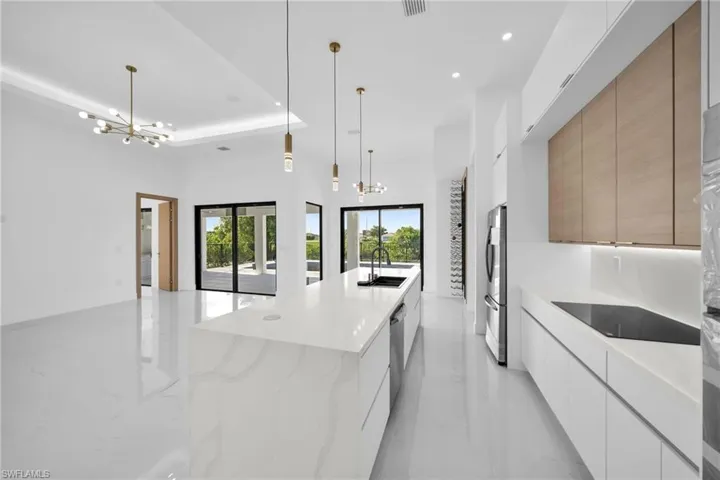 Kitchen with sink, pendant lighting, stainless steel refrigerator, light stone counters, and black electric cooktop