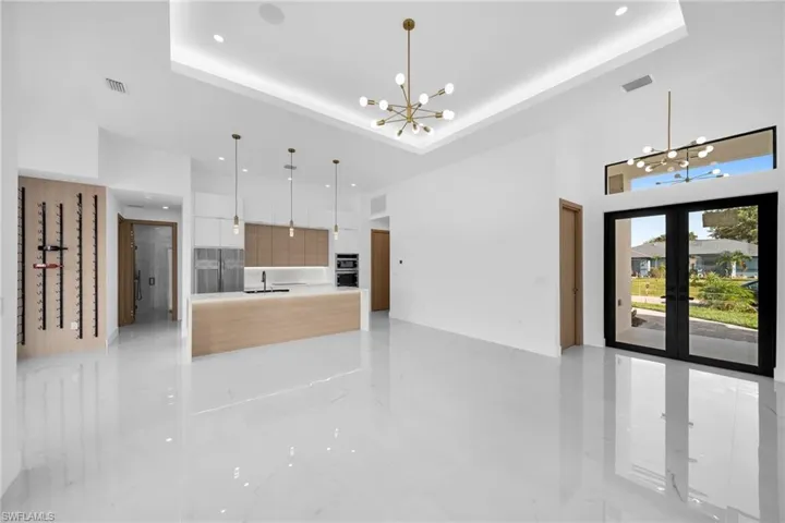 Kitchen featuring french doors, light tile patterned floors, white cabinets, a raised ceiling, and decorative light fixtures