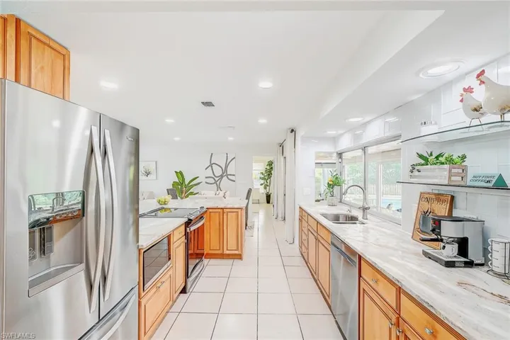Kitchen featuring light stone counters, light tile patterned flooring, sink, backsplash, and stainless steel appliances