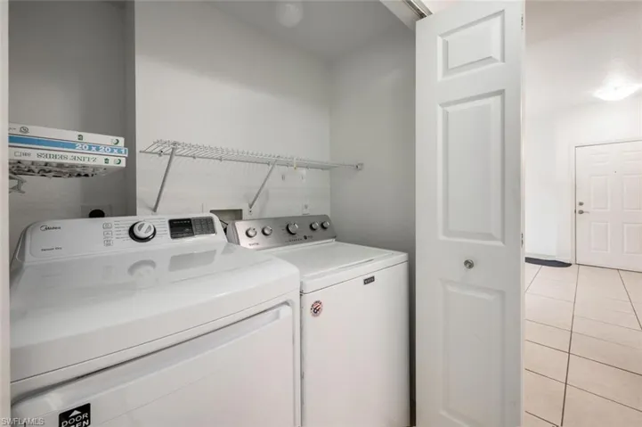 Washroom with washing machine and dryer and light tile patterned flooring