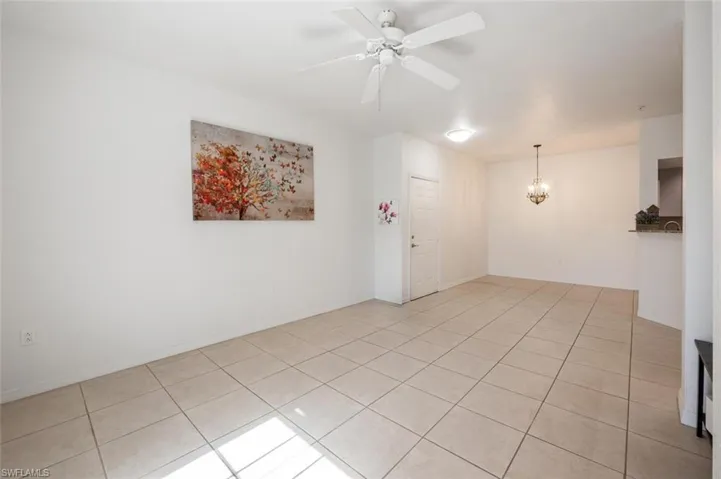 Tiled spare room with ceiling fan with notable chandelier
