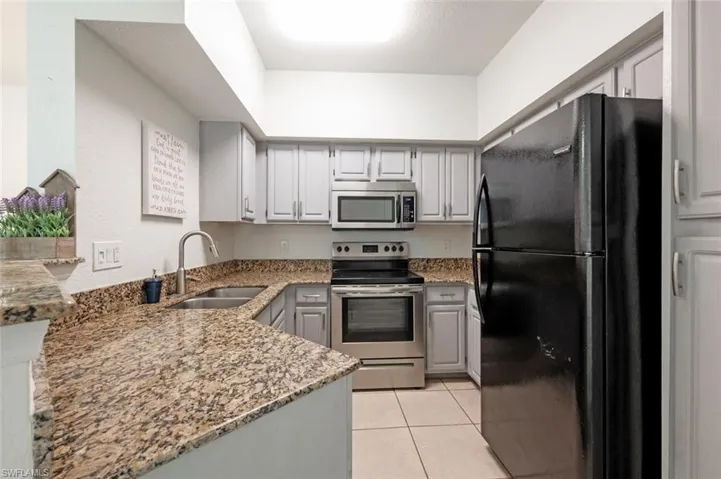 Kitchen featuring dark stone counters, gray cabinetry, stainless steel appliances, sink, and light tile patterned floors