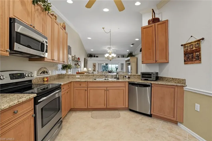 Kitchen featuring appliances with stainless steel finishes, ornamental molding, recessed lighting, light stone counters, and a ceiling fan