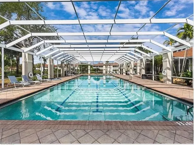 Screened lap pool  with a diving lane, surrounded by paver decking, and a privacy wall