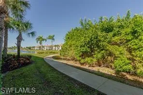Paved pathway behind unit with established landscaping, including palm trees and lush green foliage