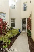 Concrete walkway entrance featuring a screen door and surrounding landscape with established plantings