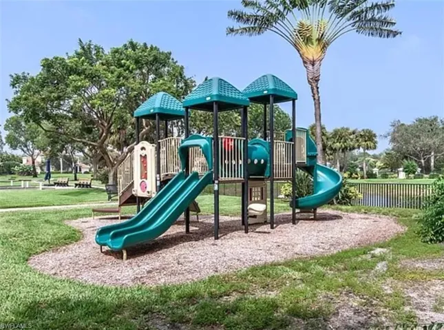 Community playground featuring multiple slides and climbing structures, surrounded by mature landscaping and a water feature