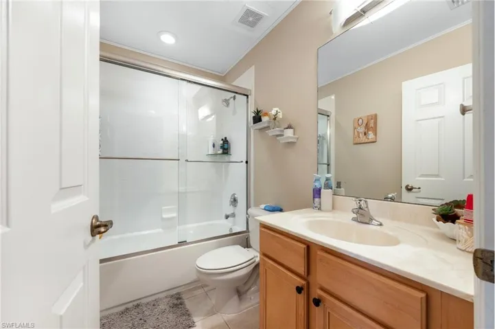 Bathroom with bath / shower combo with glass door, crown molding, vanity, and light tile patterned flooring