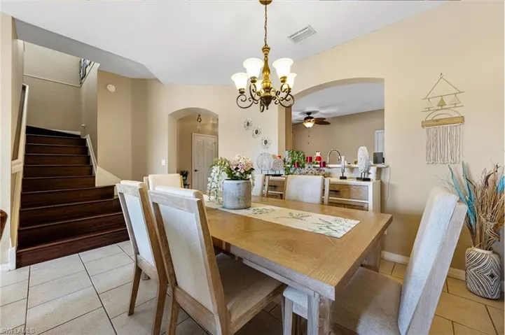 Dining area with light tile patterned flooring, arched walkways, a chandelier, and stairway