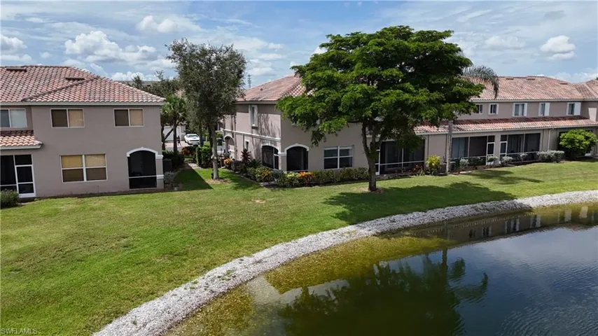 Back of house with stucco siding, a tile roof, a lawn, and a water view