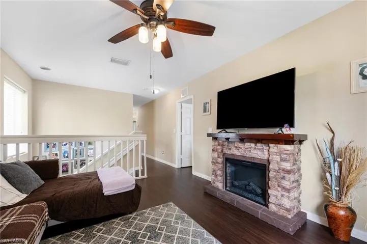 Living area with dark wood-style floors, ceiling fan, and a fireplace